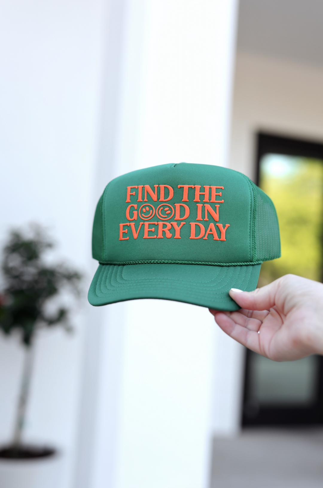 Green trucker hat with orange 'Find the Good in Every Day' embroidery, perfect for casual wear.