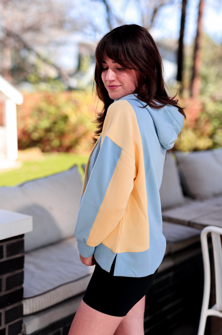 Two-tone pastel hoodie in blue and yellow, relaxed fit with a cozy hood, perfect for casual wear.