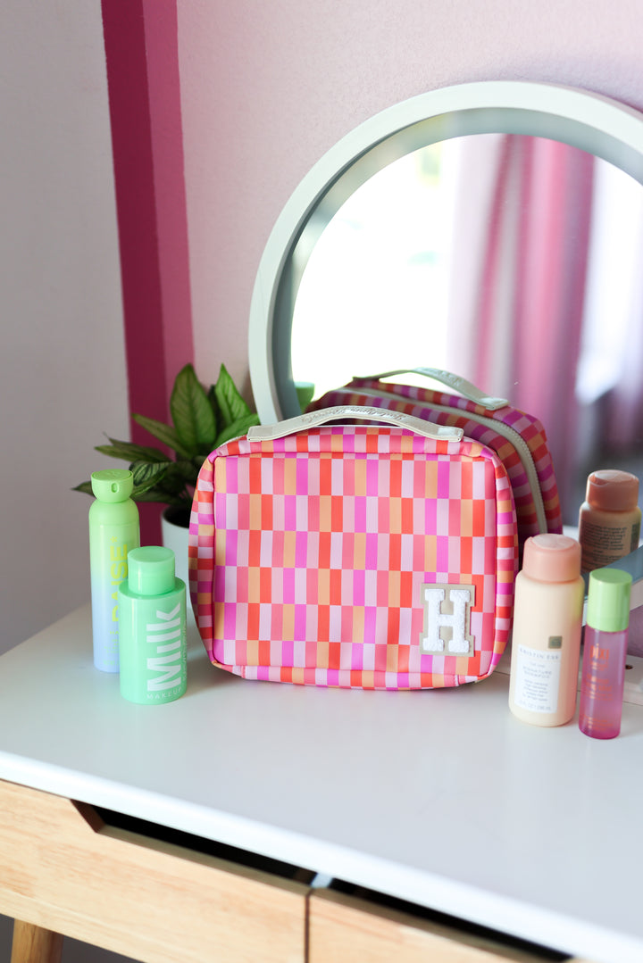 Colorful pink and orange checkered cosmetic bag with handle and embroidered letter H.