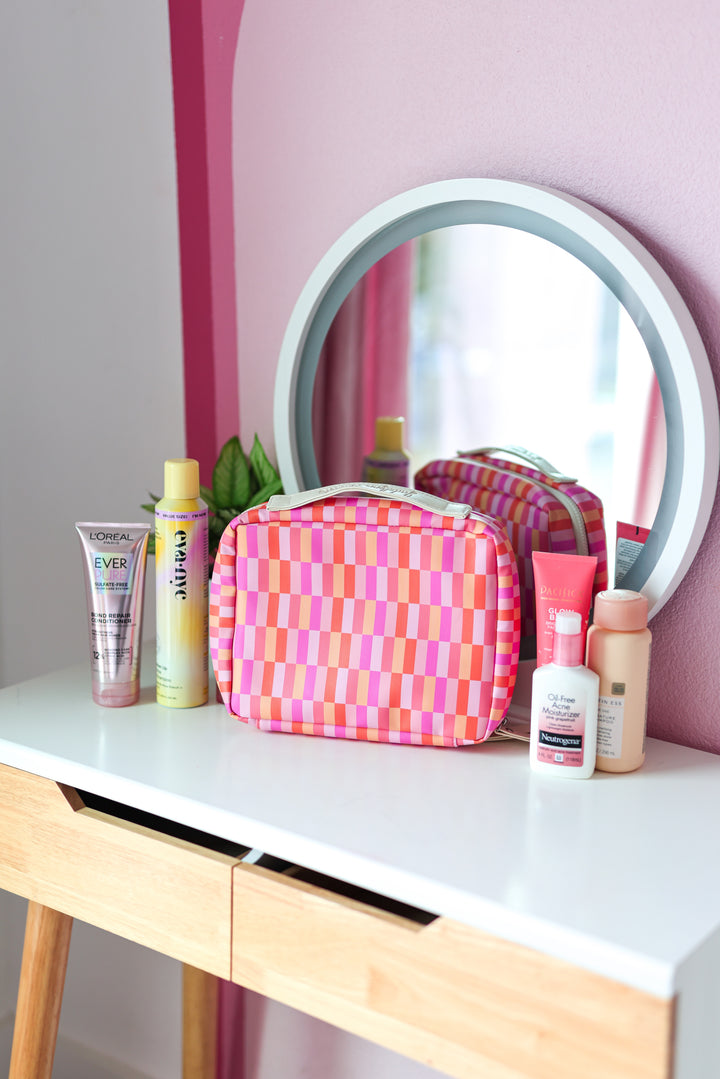 Colorful pink and orange patterned cosmetic bag on a vanity with beauty products.