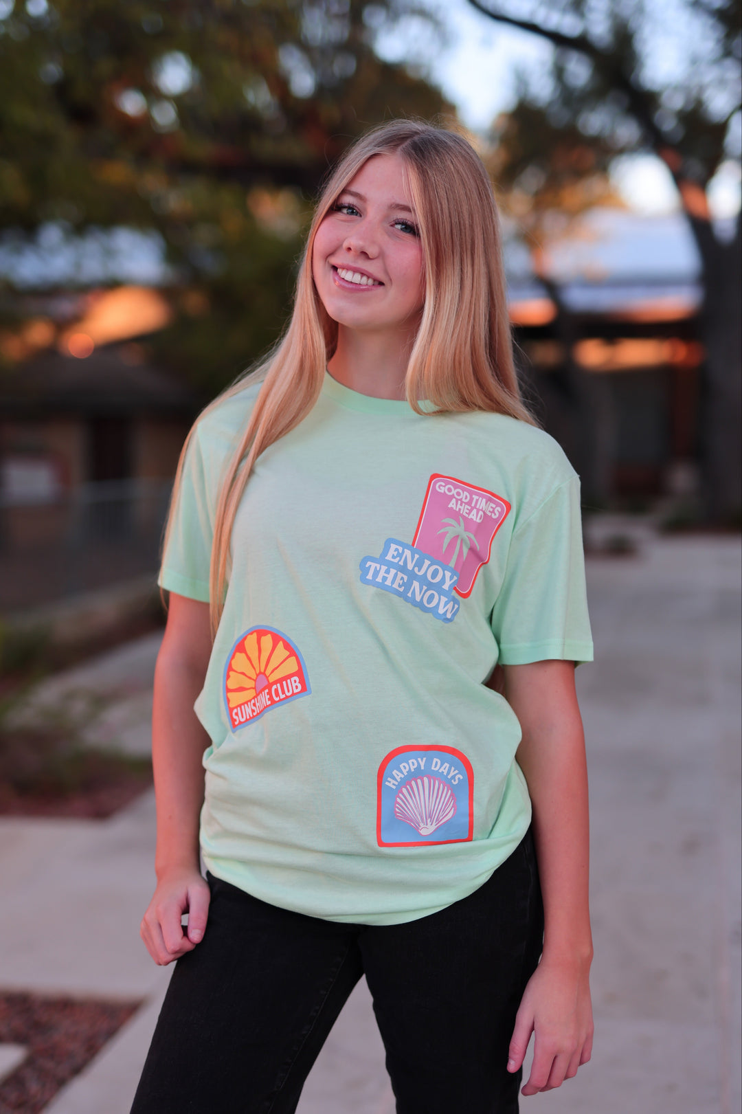 Person wearing a light green t-shirt with colorful patches outdoors