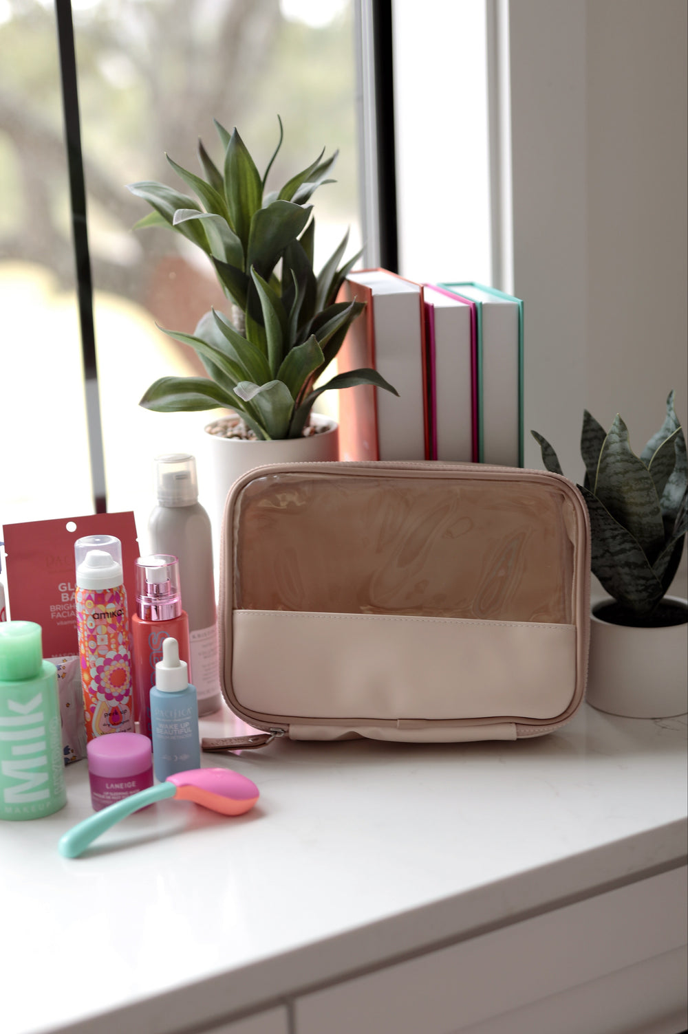 Cosmetic bag on a counter with various items including bottles and a plant in the background.