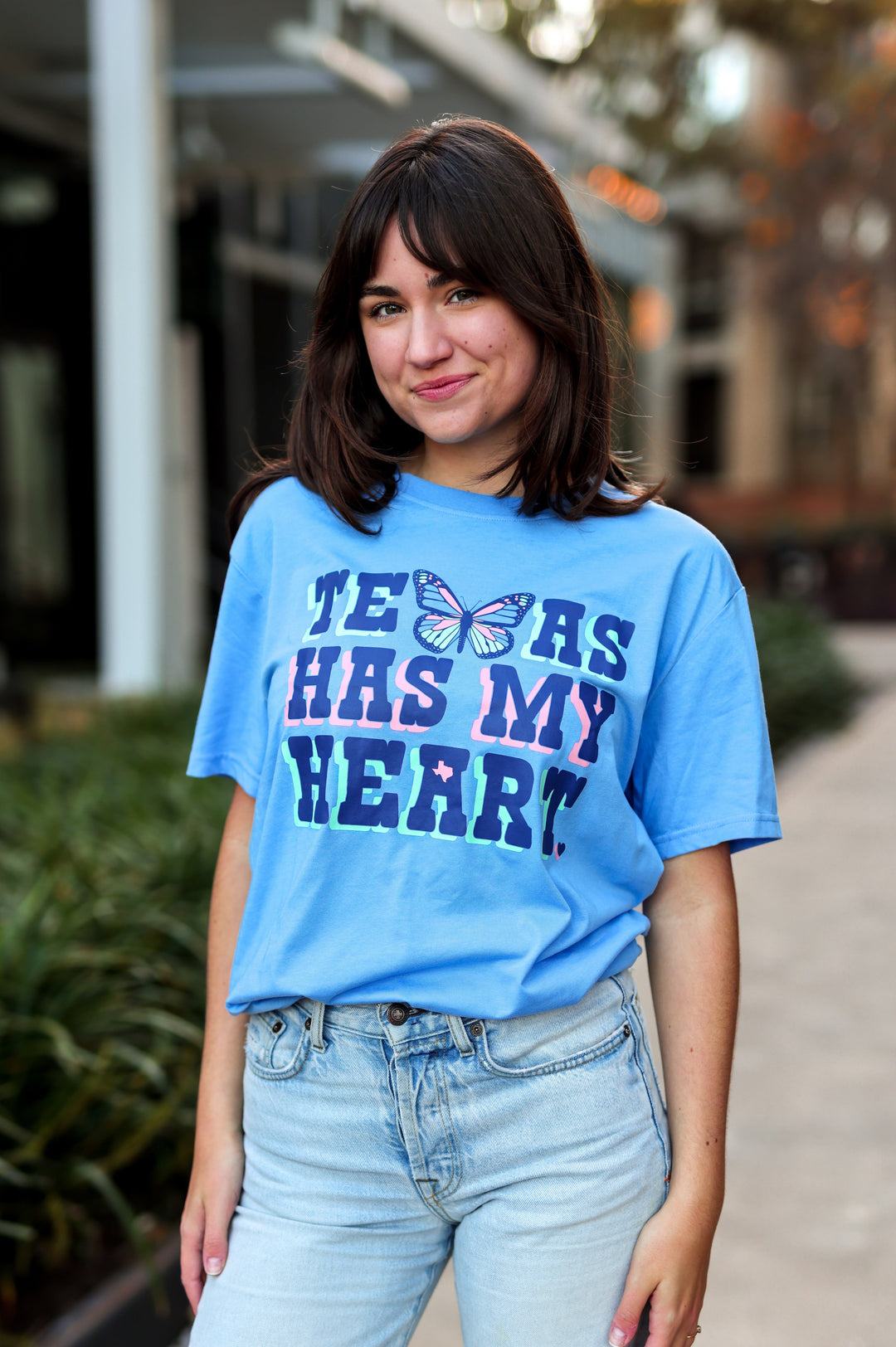 Person wearing a blue t-shirt with text standing outdoors.
