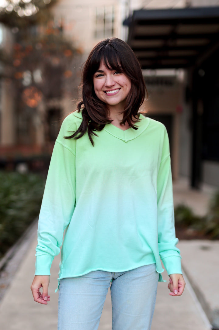 Woman wearing a green gradient sweater and light blue jeans standing on a sidewalk.