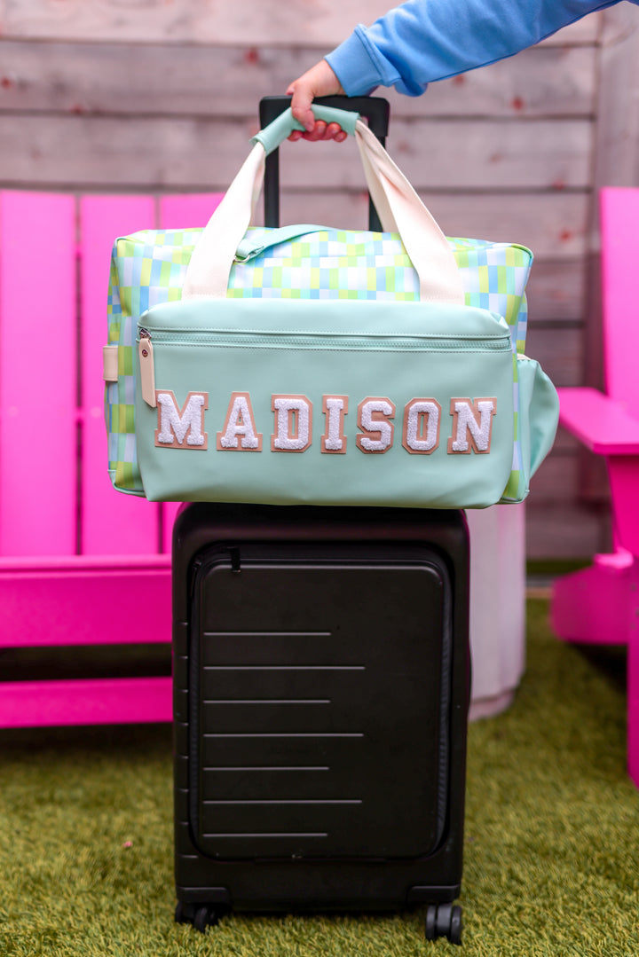 Personalized mint green travel duffel bag with green and blue pattern, resting on a black suitcase.