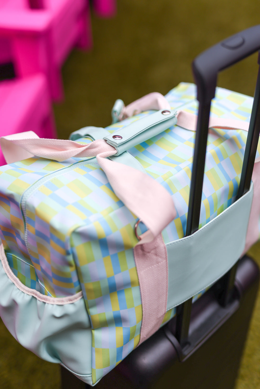Colorful plaid duffel bag with pink straps, perfect for travel or gym, attached to a suitcase.