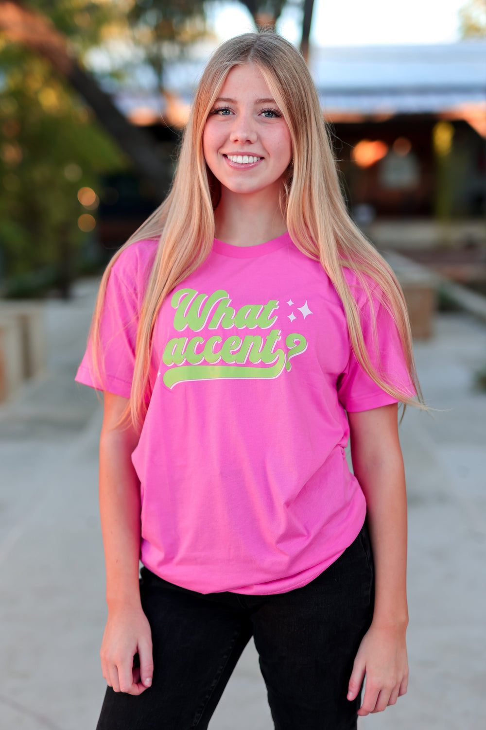 Person wearing a pink t-shirt with green text outdoors