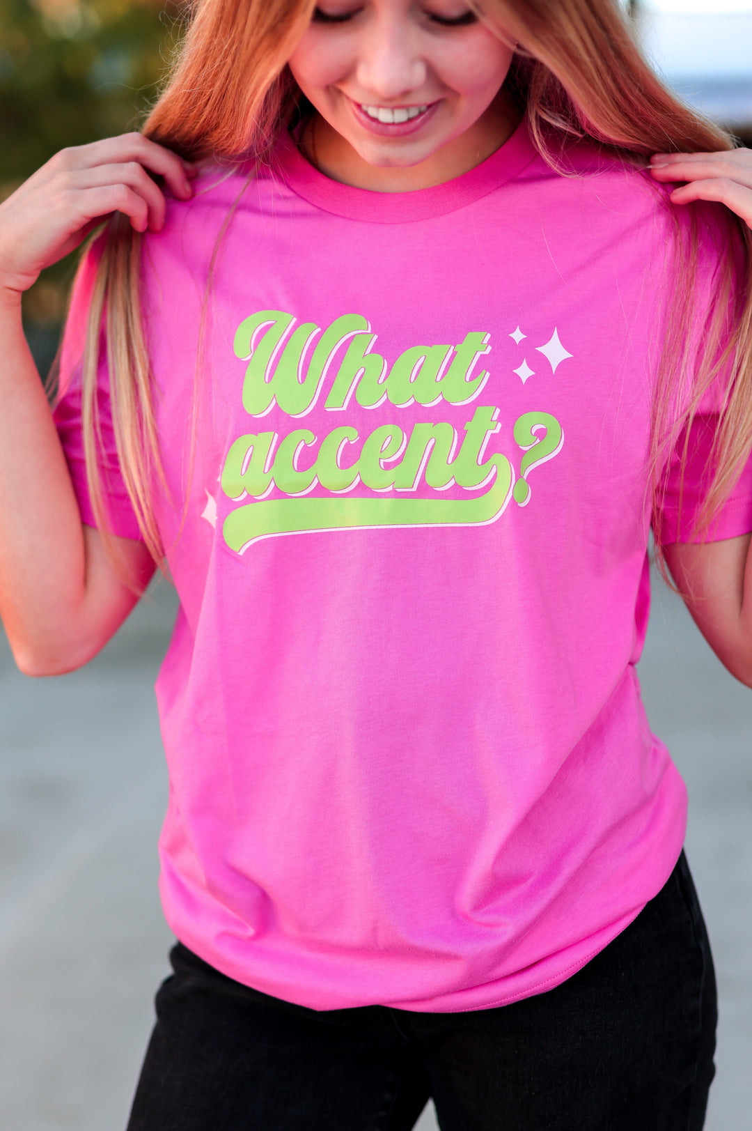 Person wearing a pink t-shirt with 'What accent?' in green text.