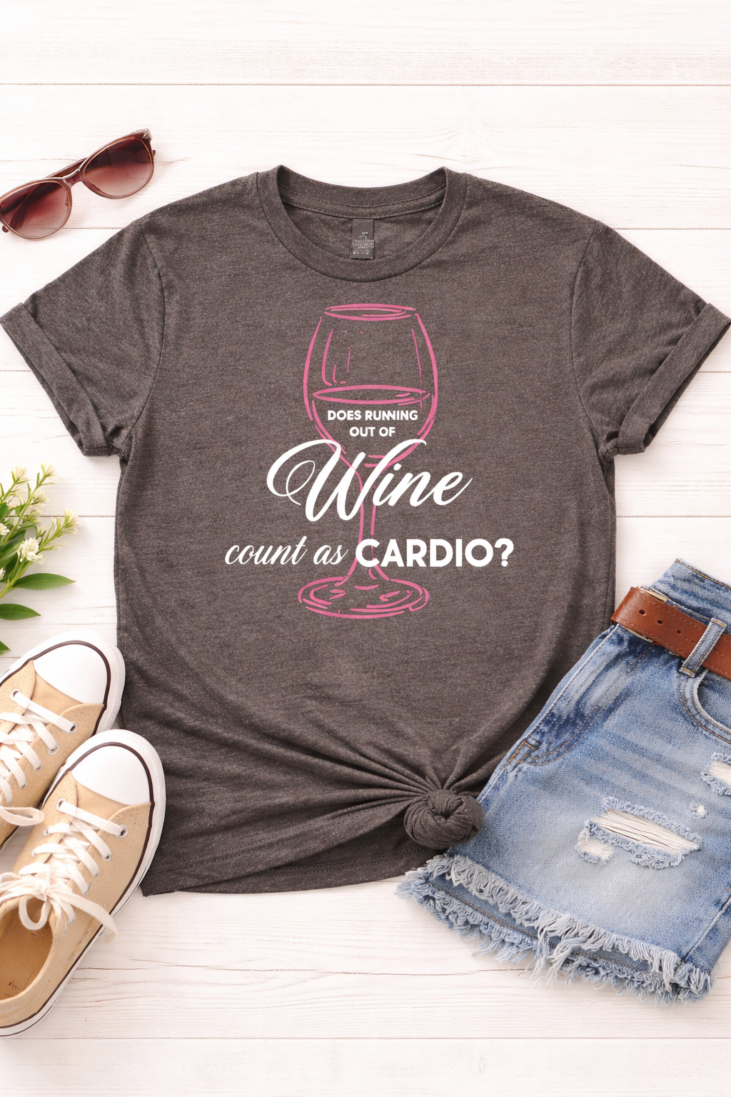 Gray t-shirt with a humorous wine graphic and text on a white surface with sunglasses, shoes, and shorts.