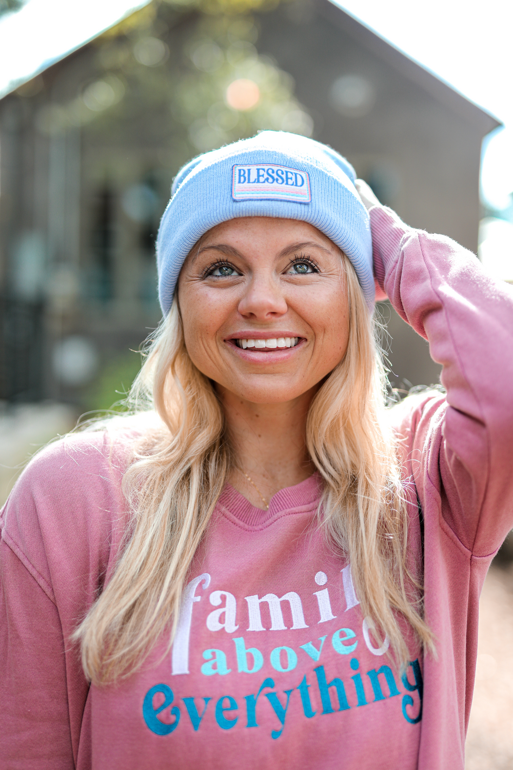 Woman wearing a light blue beanie and pink sweatshirt with 'family above everything' text.